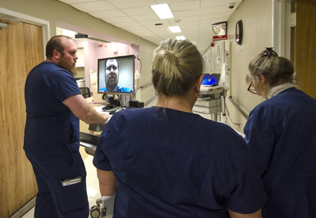 This is a picture of nurses standing in a hallway videochating another healthcare worker.